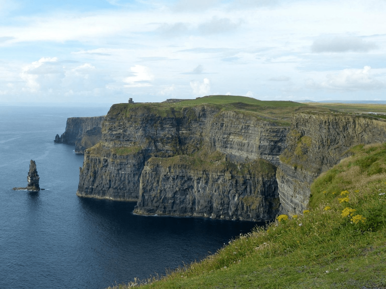 a stone bridge over a body of water with Cliffs of Moher in the background